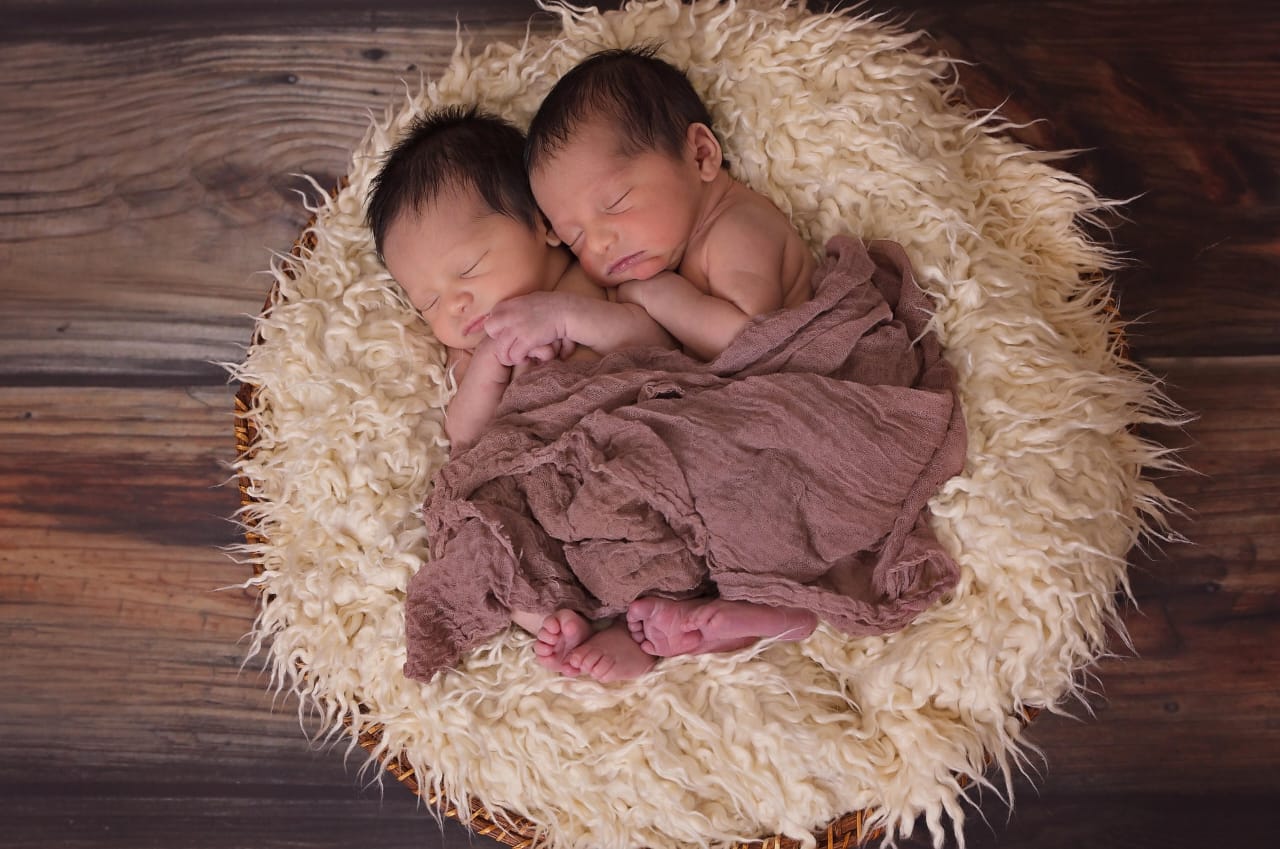 Two newborn babies peacefully sleeping wrapped in a brown cloth.