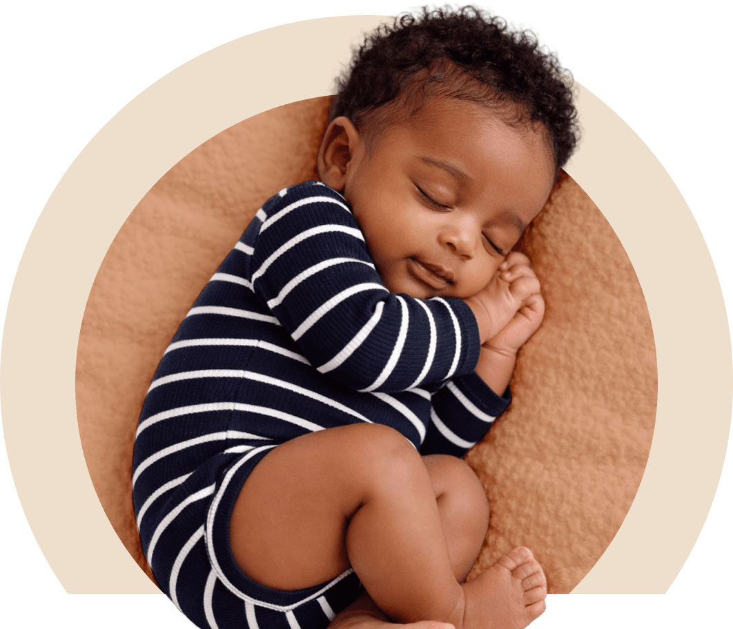 Sleeping baby in a striped onesie curled up peacefully.